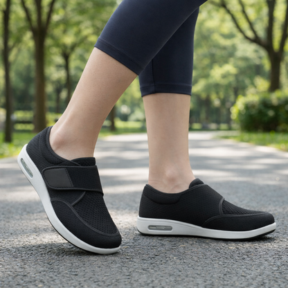 Orthopedic shoes in black with white soles worn by a person walking on a paved park path.