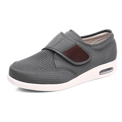A gray orthopedic shoe shown from the side featuring a textured upper and an adjustable strap with a brown accent.