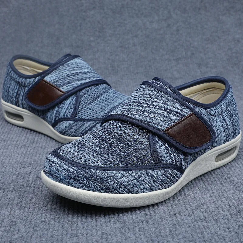 Orthopedic shoes in a light blue heathered mesh with brown strap accents resting on a gray surface.