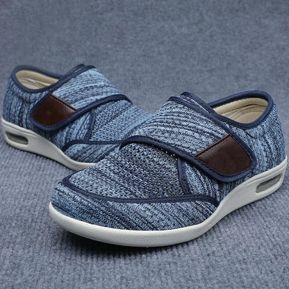 Orthopedic shoes in a light blue heathered mesh with brown strap accents resting on a gray surface.