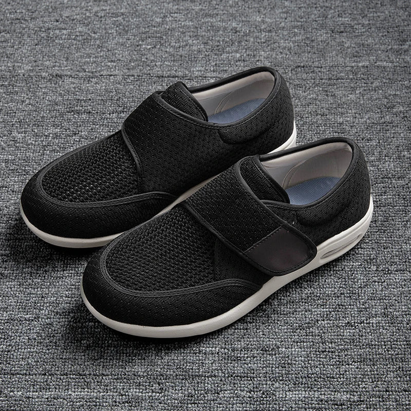 StepMax orthopedic shoes with a black mesh upper and adjustable velcro straps resting on a gray textured surface.