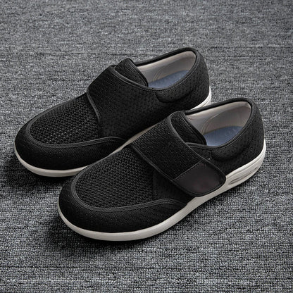 StepMax orthopedic shoes with a black mesh upper and adjustable velcro straps resting on a gray textured surface.